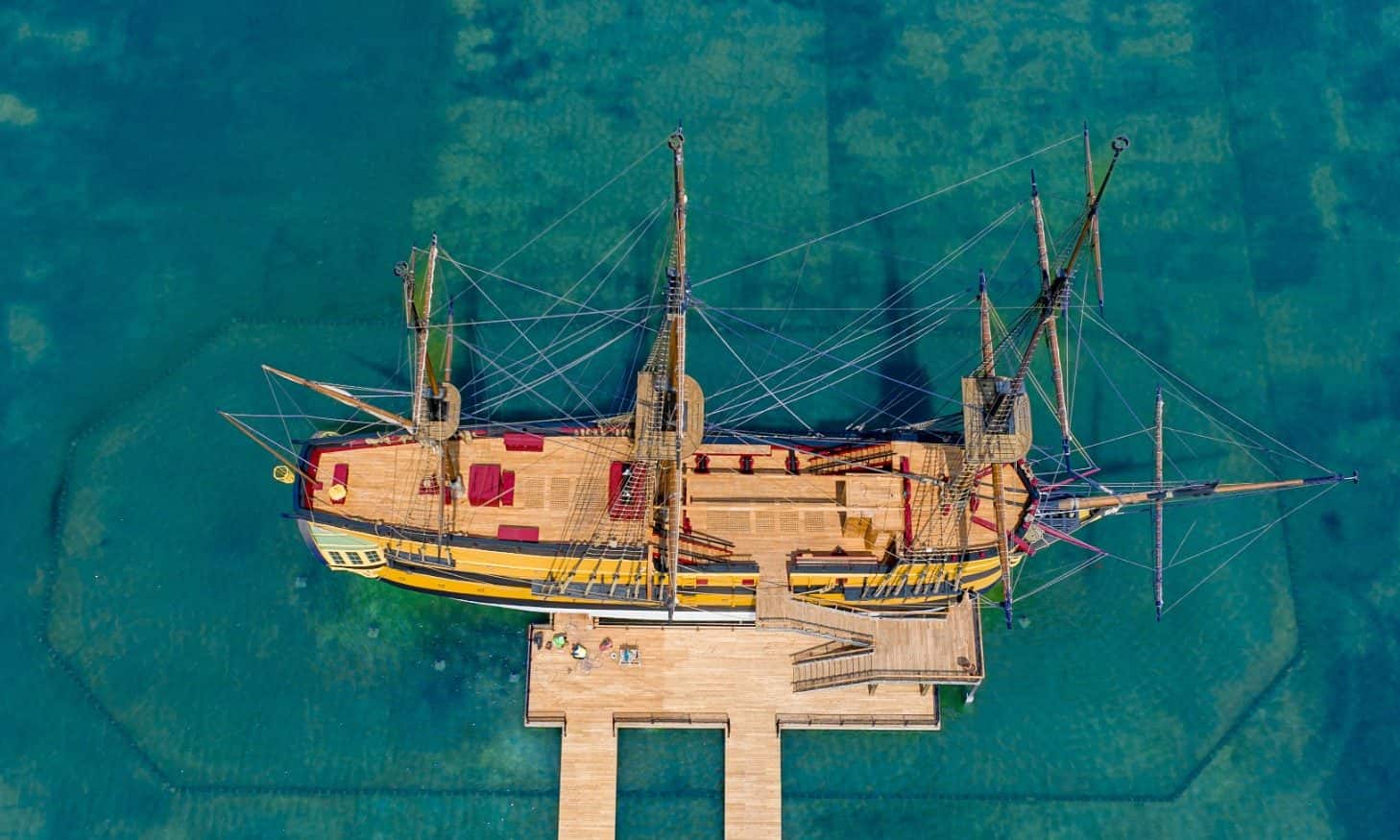 Vue aérienne d'un trois-mâts amarré à un ponton de bois, dans une eau turquoise peu profonde