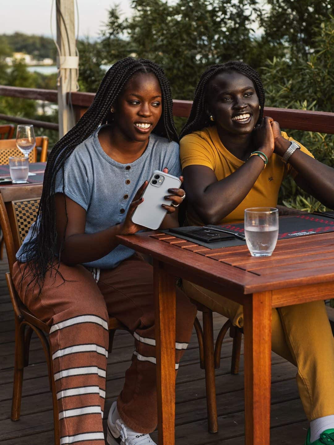 Deux amies comparent des adresses sur un même téléphone, attablées en terrasse