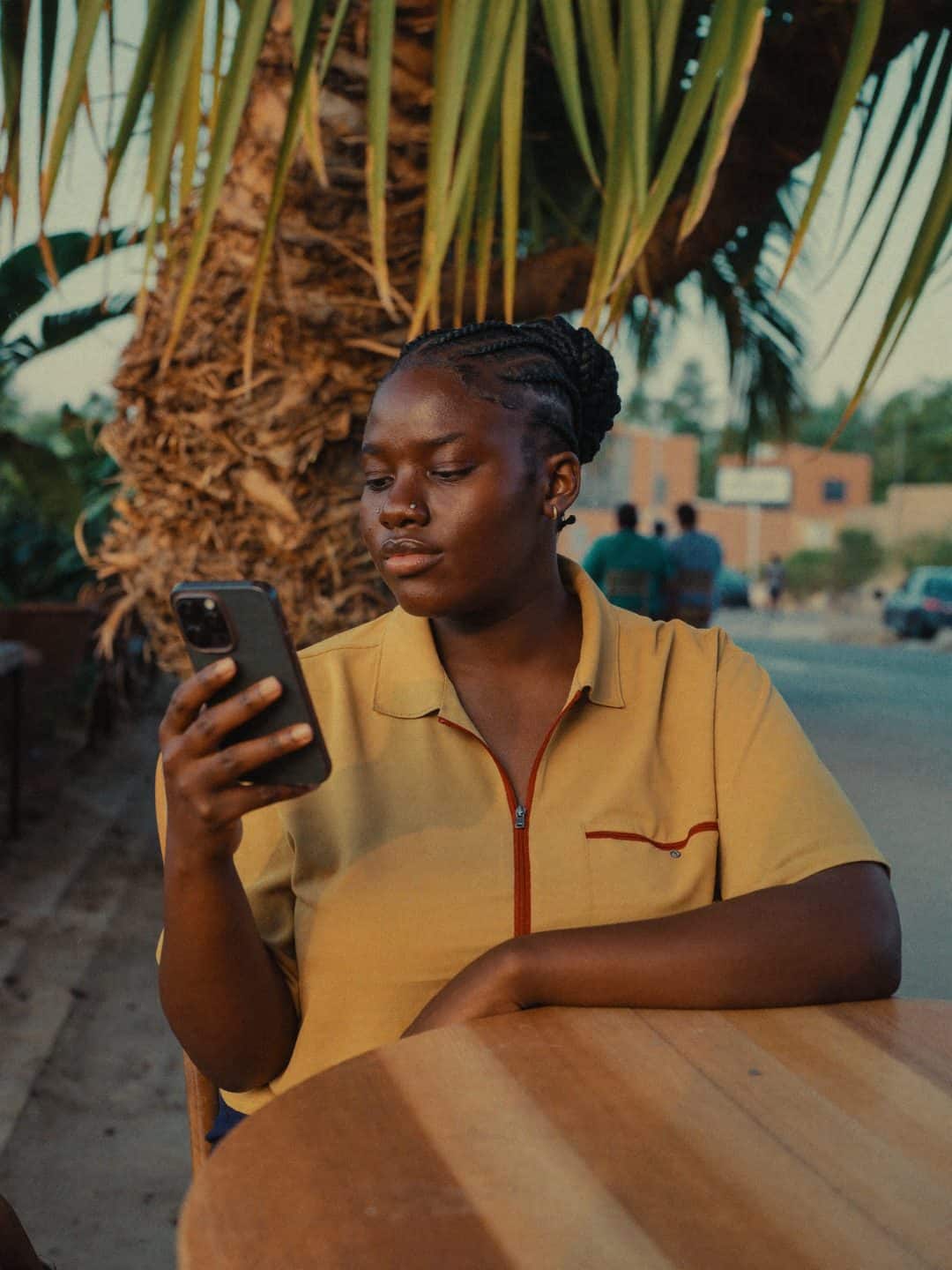 Une jeune femme consulte son téléphone à la terrasse d'un café, à la tombée du jour