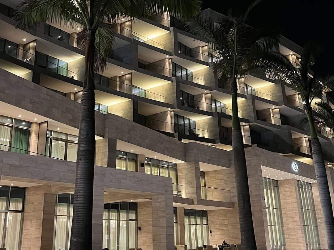 Façade d'hôtel éclairée la nuit, balcons et palmiers